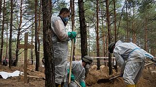 Arbeiter stehen auf dem Waldfriedhof von Isjum am Grab eines nicht identifizierten Zivilisten. Foto: Evgeniy Maloletka/AP/dpa