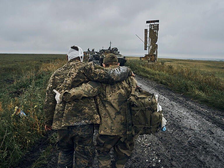 Ein ukrainischer Soldat hilft einem verwundeten Kameraden auf der Straße in dem befreiten Gebiet in der Region Charkiw, Ukraine. Foto: Kostiantyn Liberov/AP/dpa