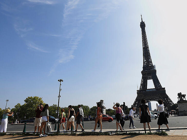 Touristen besichtigen und fotografieren den Eiffelturm. Foto: Aurelien Morissard/AP/dpa