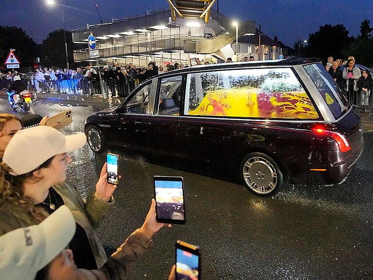 Menschen nehmen mit ihren Handys den Leichenwagen mit dem Sarg von Königin Elizabeth II. auf dem Weg vom Luftwaffenstützpunkt Northolt zum Buckingham Palace auf. Foto: Martin Meissner/AP/dpa