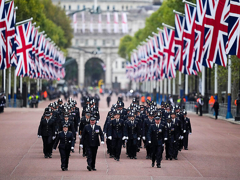 Polizeibeamte gehen vor der Staatsakt zur Beisetzung von Königin Elizabeth II. über die Prachtstraße The Mall. Foto: Vadim Ghirda/Pool AP/dpa