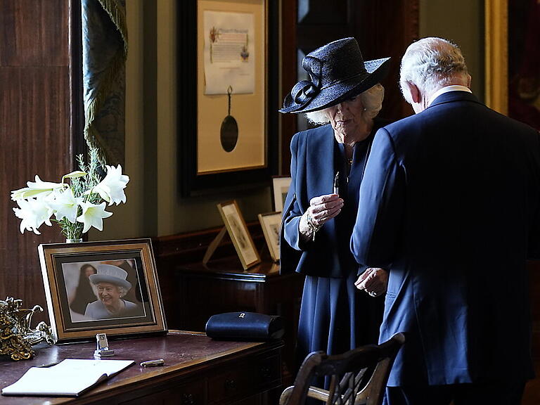 Camilla hält einen Füllfederhalter, während sich König Charles III. Tinte von der Hand wischt. Foto: Niall Carson/PA Wire/dpa